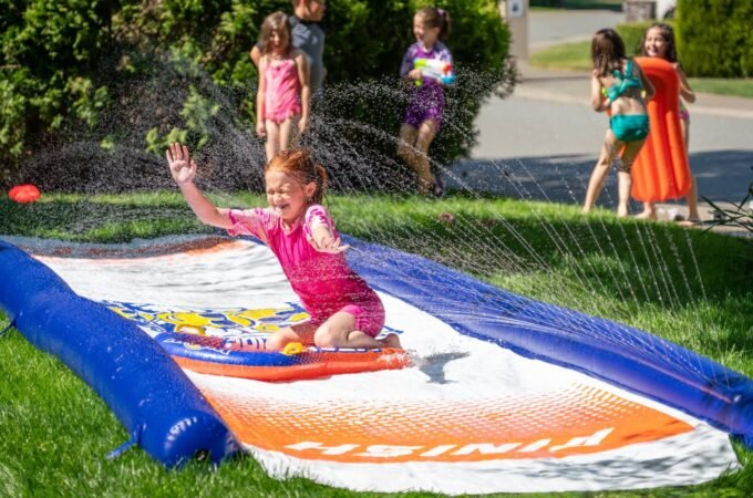 Children playing on an inflatable slip and slide in a backyard sprinkler setup.