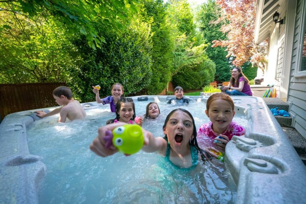 A group enjoying a hot tub filled with bubbly blue water, surrounded by lush greenery and a backyard setting.