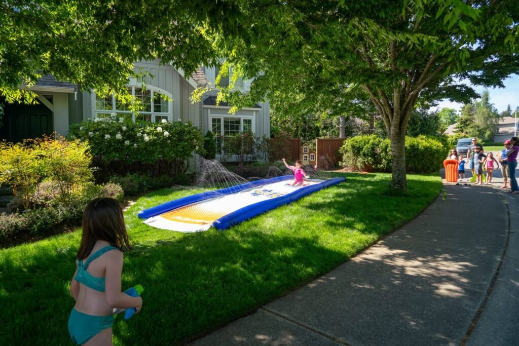 A water slide on a sunny day with people enjoying summer activities in a lush green backyard.