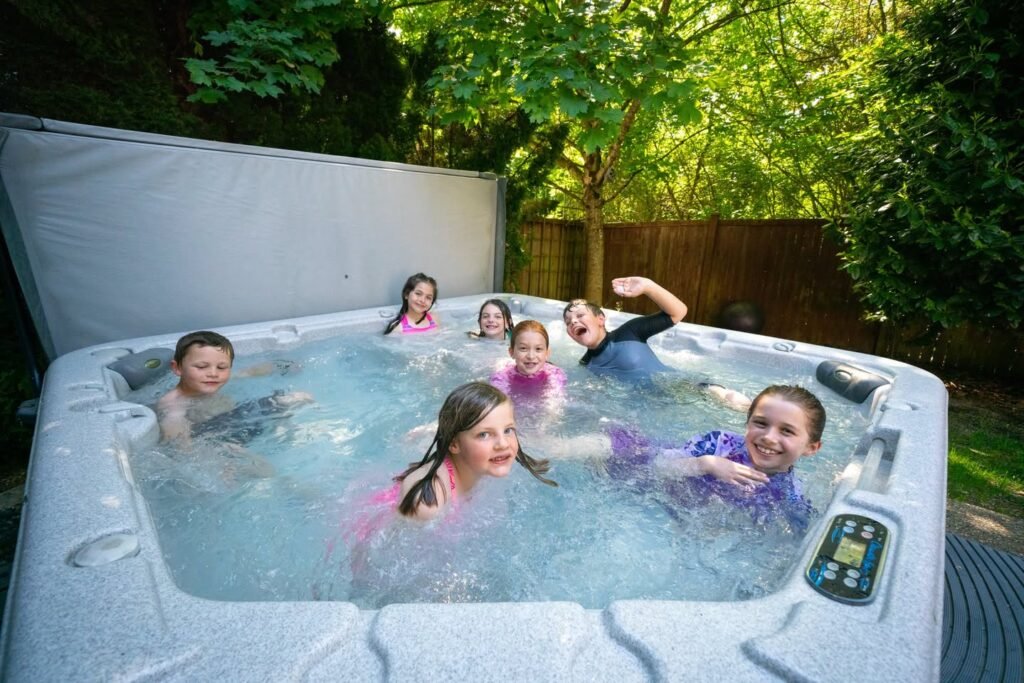 Children enjoying a spa in a backyard with a hot tub cover nearby. Lush green trees surround the private outdoor space.