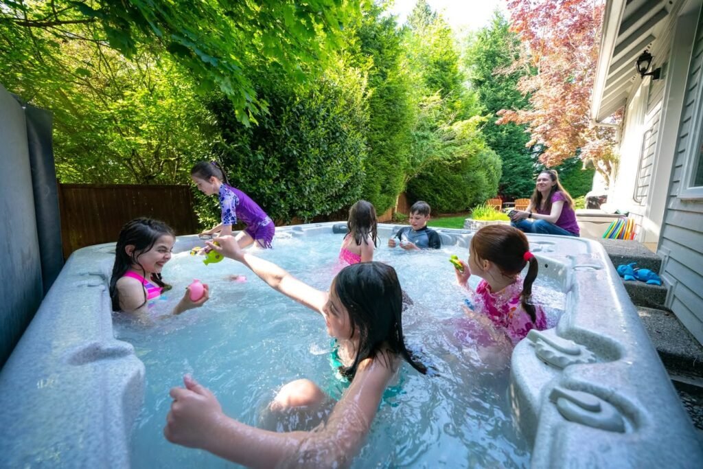 Children enjoying a backyard hot tub with lush greenery and a house in the background.