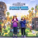 Two visitors standing in front of a Minecraft MineFaire promotional display. The background features blocky pixel art and gaming characters.