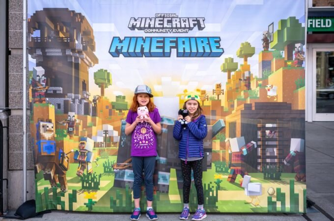 Two visitors standing in front of a Minecraft MineFaire promotional display. The background features blocky pixel art and gaming characters.