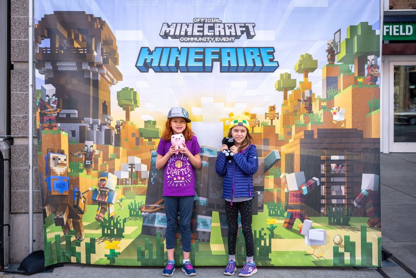 Minefaire Two visitors standing in front of a Minecraft MineFaire promotional display. The background features blocky pixel art and gaming characters.