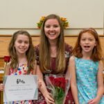 Minefaire Three individuals posing with a flower and certificate in front of a wooden upright piano.