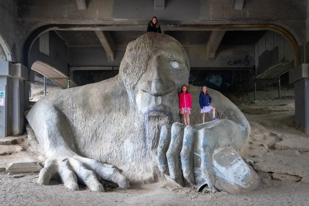 Visitors explore the detailed giant sand sculpture of a seated figure resting a hand on its face at Atlas, The Globe. A larger human figure looks on from the surrounding architectural archways in this sand art exhibit.