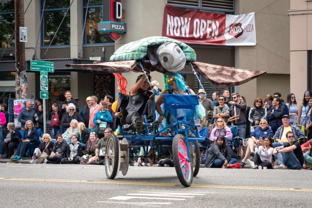 A decorated float with a large turtle-like face moves down a street lined with spectators.