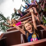 Cascade Falls Group of excited people with raised hands enjoy a roller coaster ride outdoors.