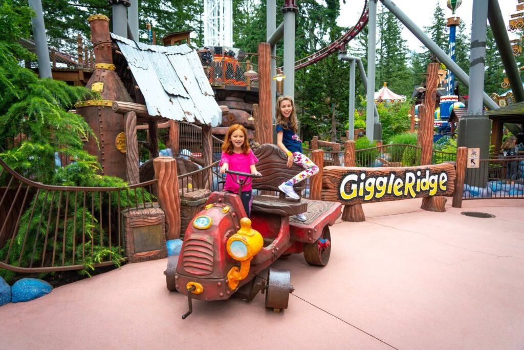A whimsical vehicle in the Giggle Ridge themed area with children posing next to it.