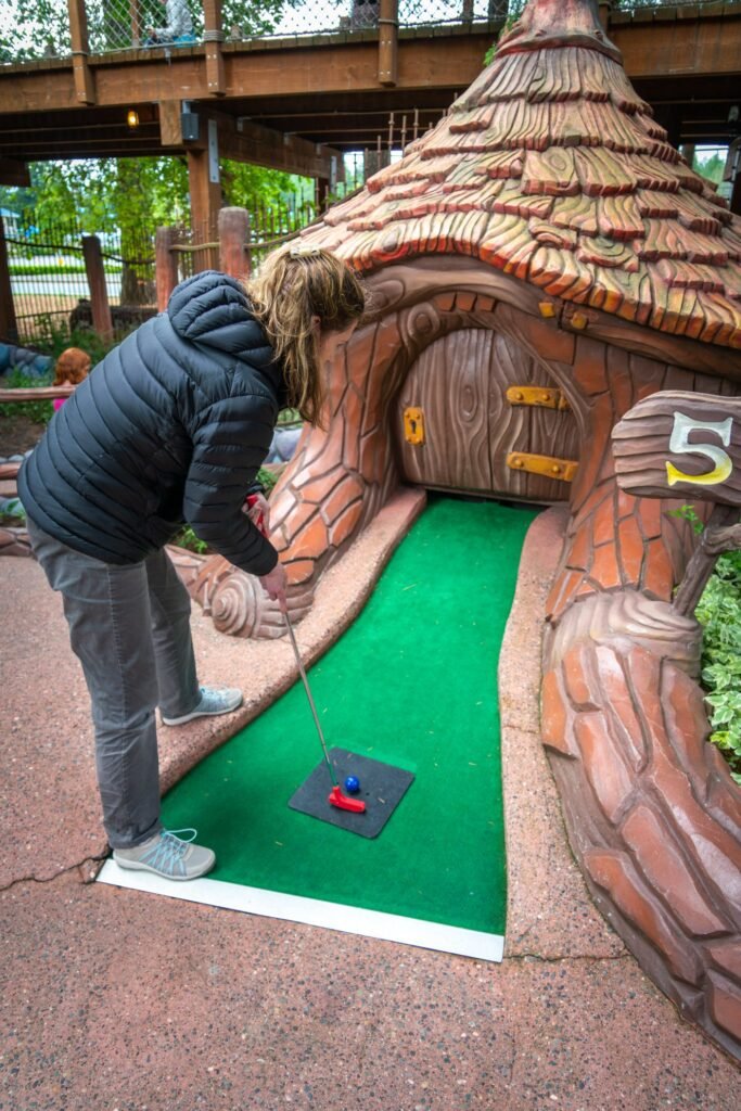 A person plays a shooting-themed mini-golf hole with a rock texture and green putting surface.