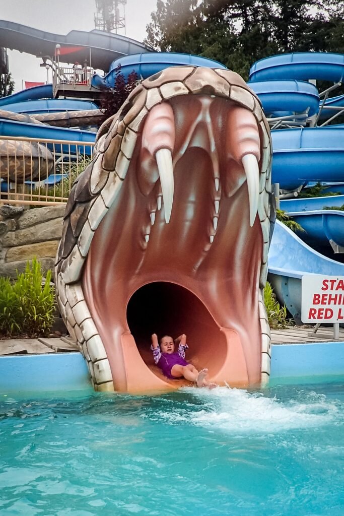 Two people splashing through a large beast-themed water slide exit into a pool.