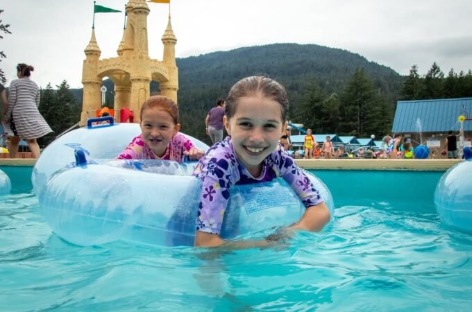 Two children enjoy a splash in a pool with castle-like structures and mountains in the background.