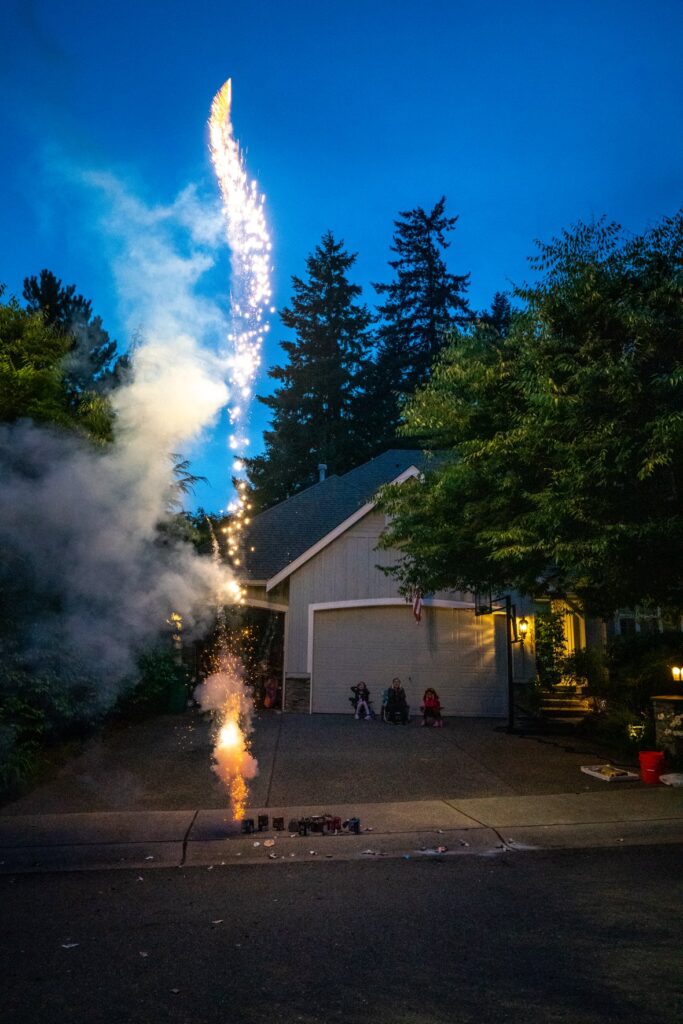Catching a moment of fireworks ignition in the driveway of a home. Watching the bright streak of light shoot up into the darkening blue sky.