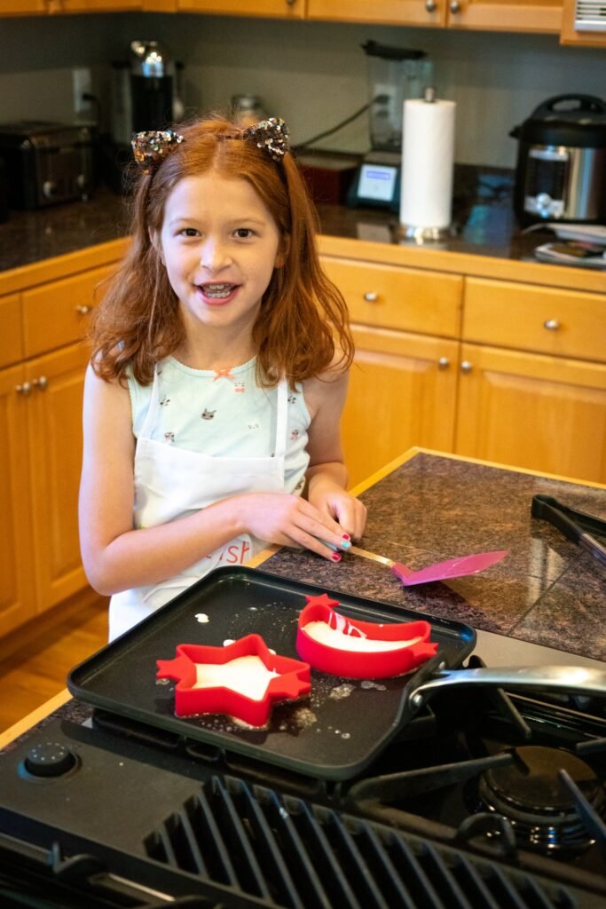 A smiling girl in the kitchen holding red molds for cooking.