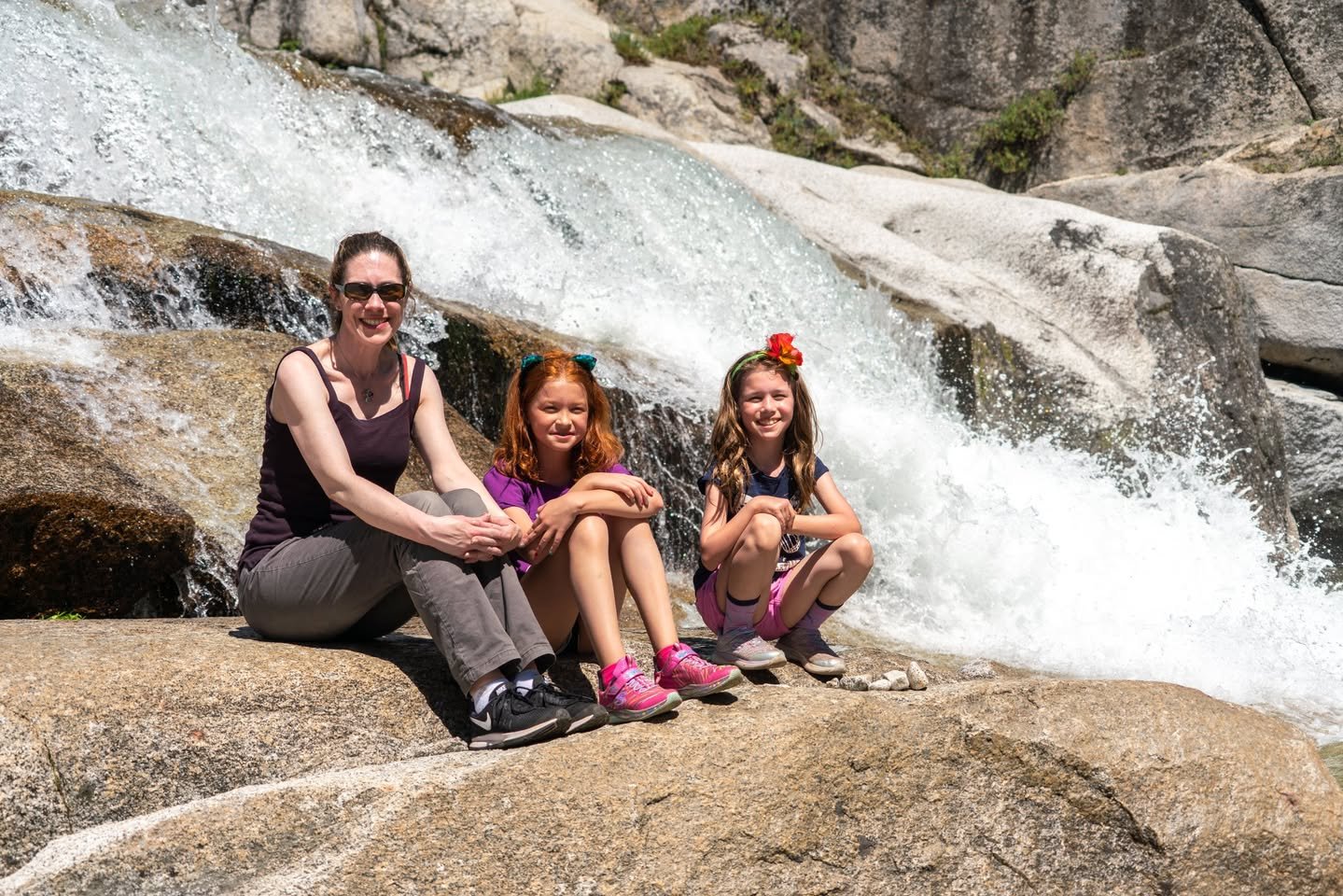 A family relaxes on smooth boulders while a waterfall tumbles over the rocks behind them.