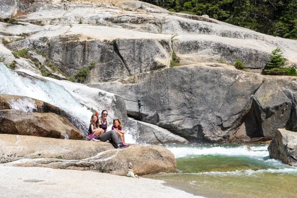 people sitting on rocks beside a small waterfall in a rocky natural setting