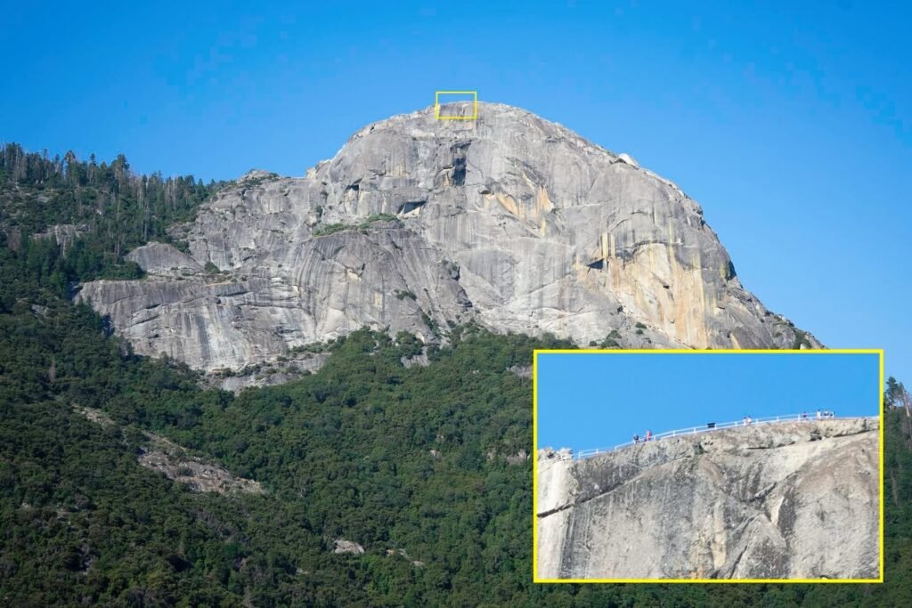 A high-altitude cliffside view framed by a blue sky and lush green trees.