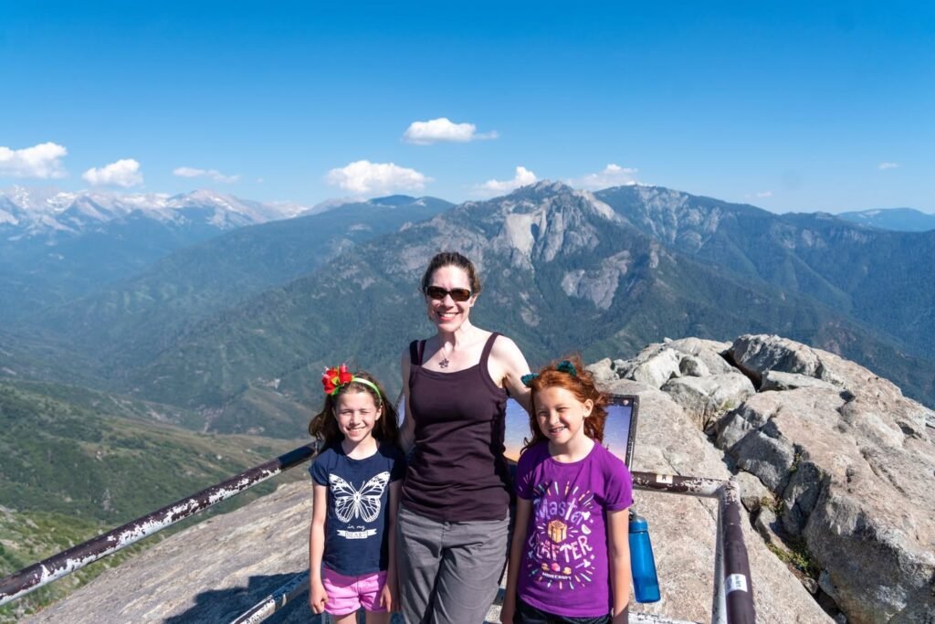 A family enjoying a mountain top view with scenic peaks and blue skies.