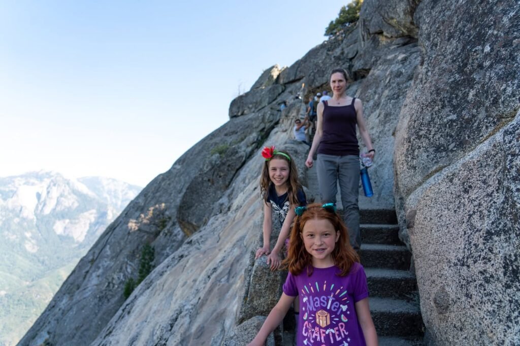 A family hikes on a steep granite slope with concrete steps carved into the rock in a mountainous area.