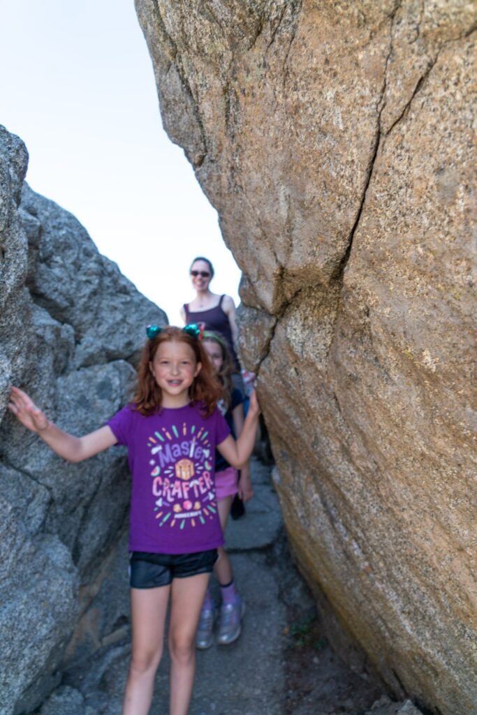 A child poses between large rocks while others explore the scenic area in the background.