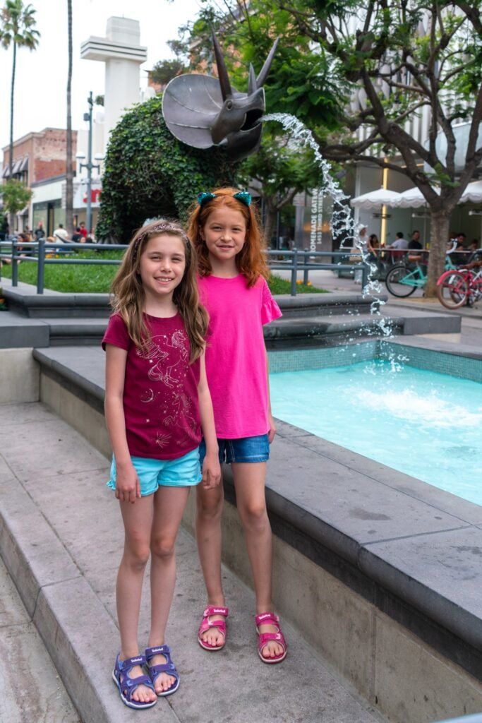Two children standing in front of a fountain with a whimsical sculpture.
