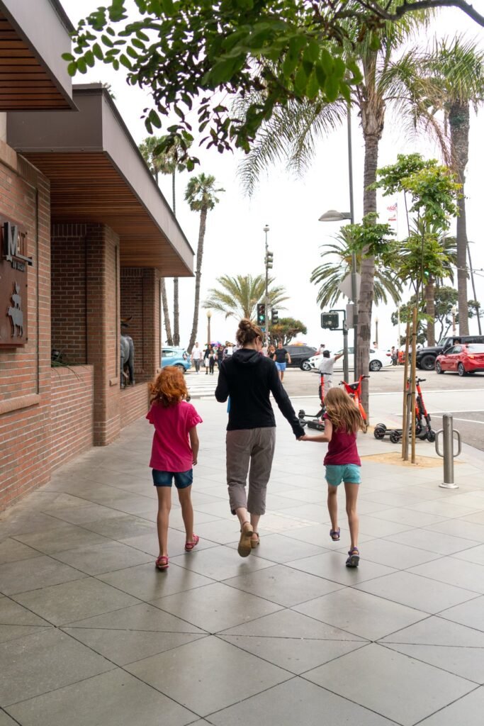 A group of people walking hand in hand along a wide plaza lined with palm trees and brick buildings.