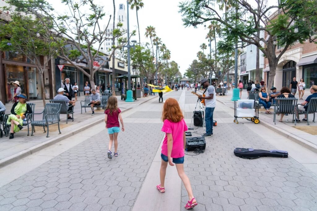 Children walking near a street performer on a brick pathway. A guitar case lies close by for tips during the outdoor show.