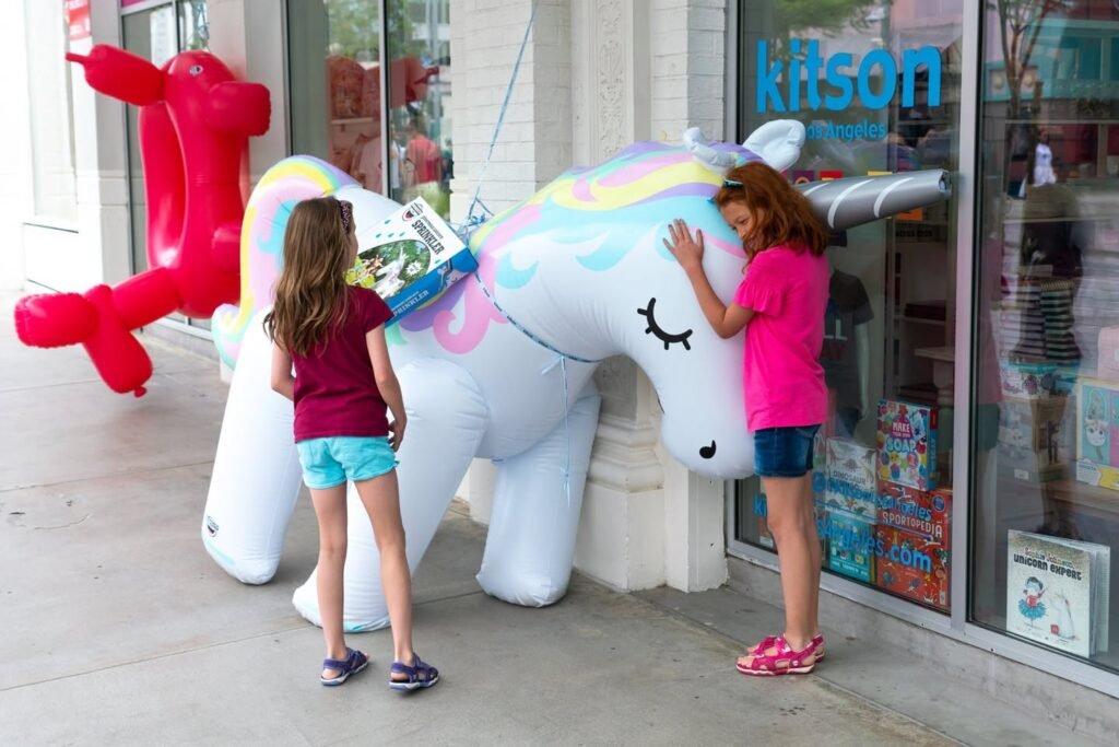 A child touches an inflatable unicorn and red dog outside the Kilson store, capturing a joyful family moment in the Pacific Northwest.