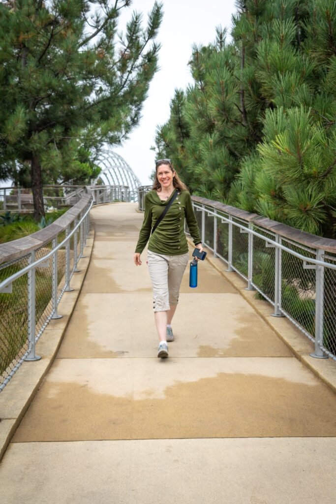 A person walks a boardwalk lined with lush coniferous trees. The scene features a serene Pacific Northwest setting.