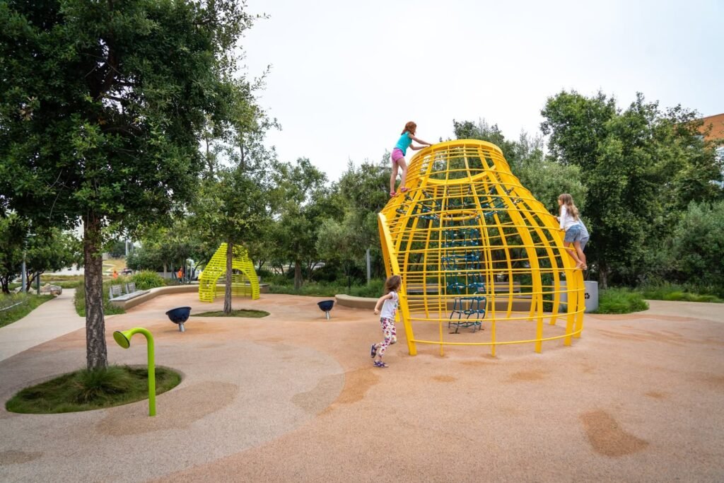 Children exploring a large yellow climbing dome on a sandy playground.