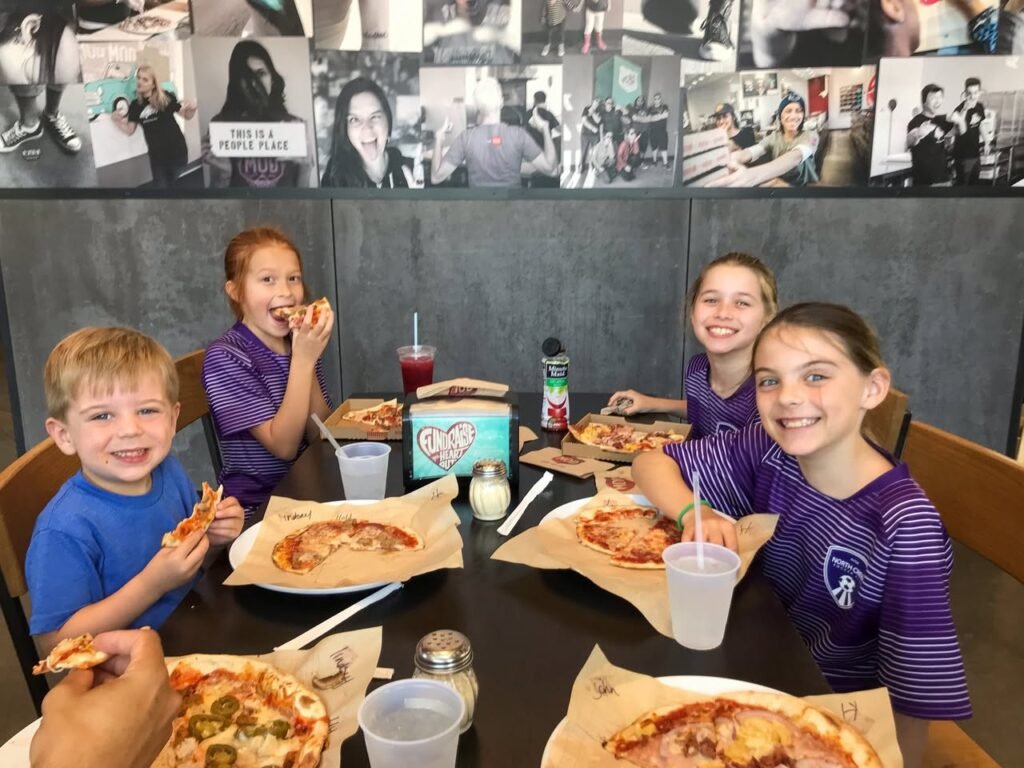 Children and adults enjoying a pizza meal at a casual restaurant with a photo-covered wall.
