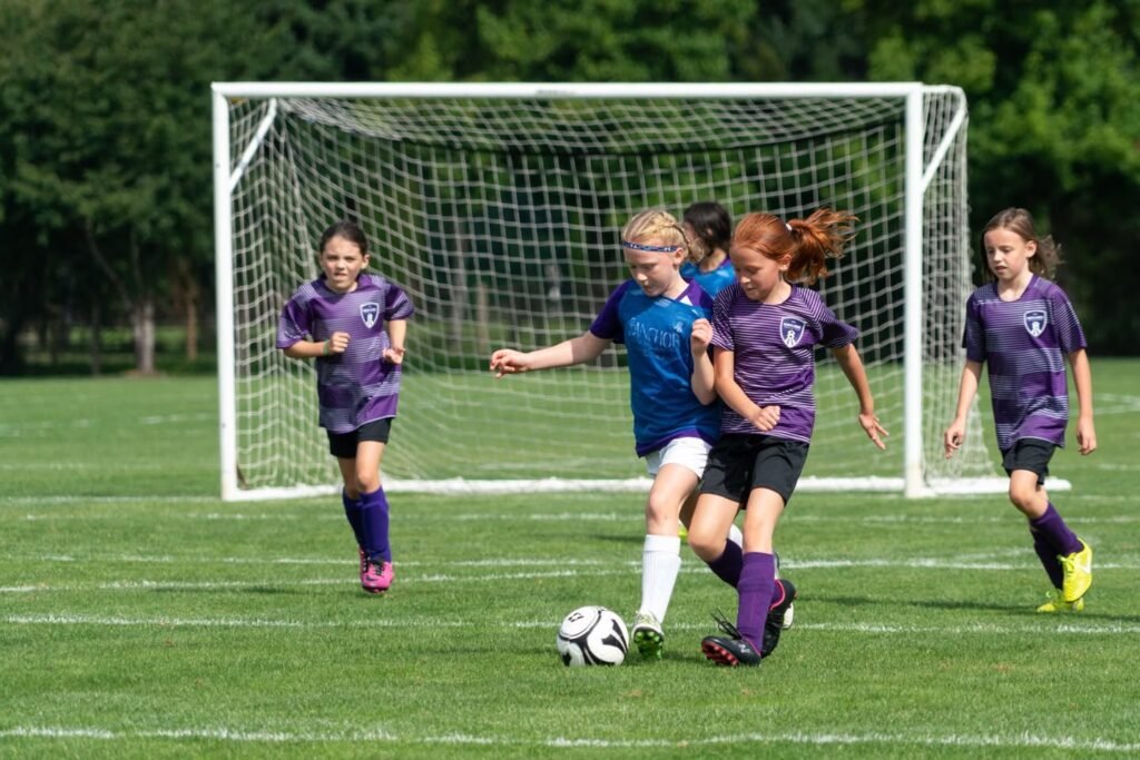 Young athletes compete for the ball in a vibrant purple and blue youth soccer game on a green field.