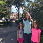 Family walking through a historic hotel courtyard on a sunny day. Green trees and people gathered on the grounds.