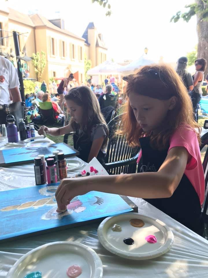 Children painting at an outdoor event with colorful supplies.