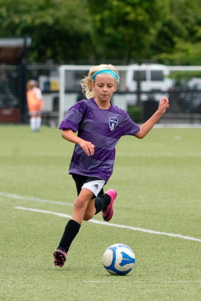 Young soccer player chasing a ball in a purple jersey on a green field.