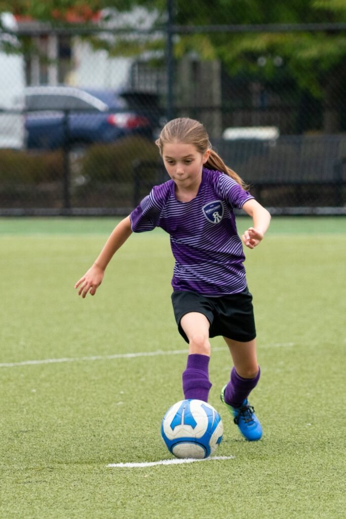 A youth athlete in a purple jersey skillfully controls a soccer ball on a green field.