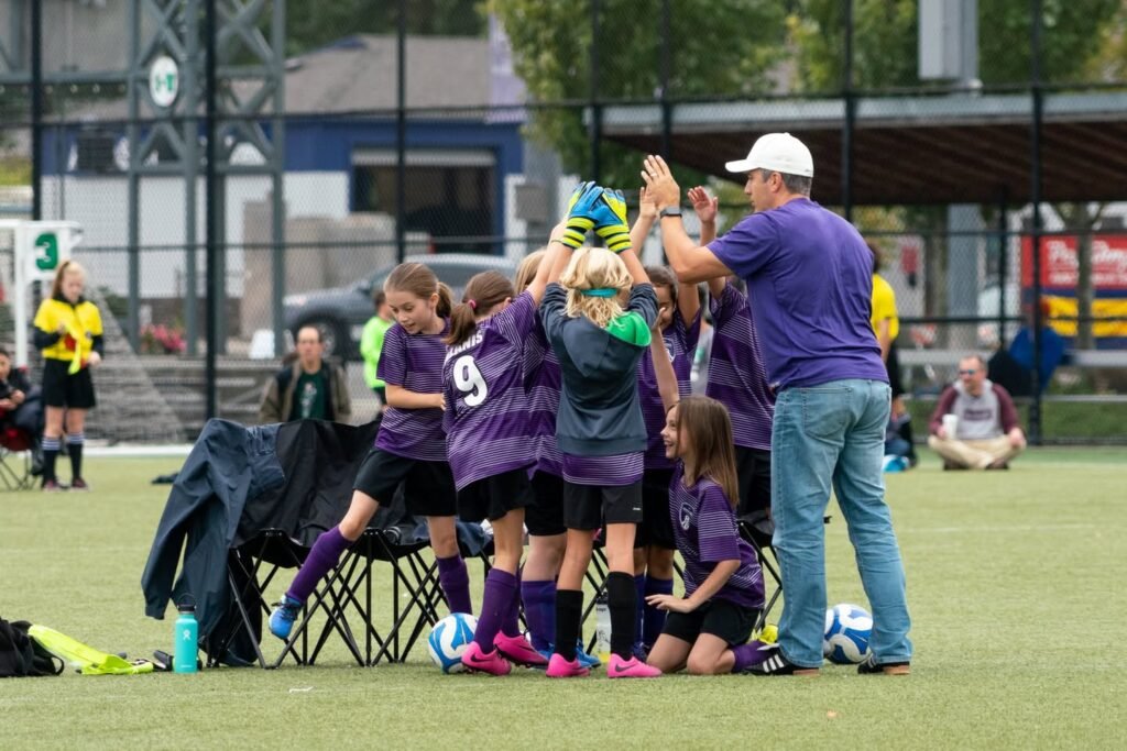 A group of young soccer players celebrates with a coach during a match.
