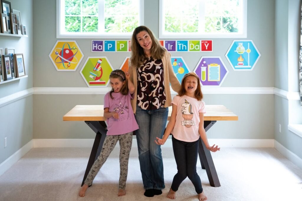 A woman and two young children pose in a bright room with hexagonal wall art and built-in desks.