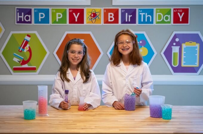 Children in lab coats conduct colorful experiments at a Happy Birthday display.