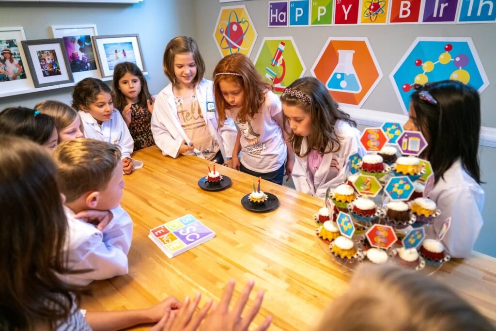Children in white lab coats engage in a hands-on science craft or experiment at a table.