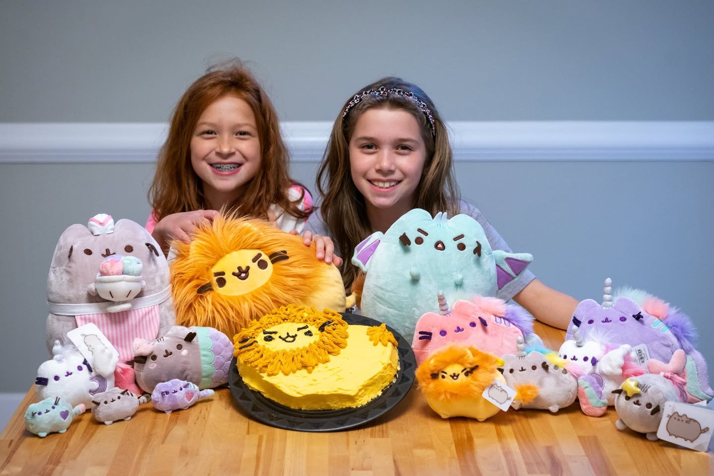 Pusheen’s Birthday Two smiling girls sitting behind a table filled with colorful bakery-themed plush toys.