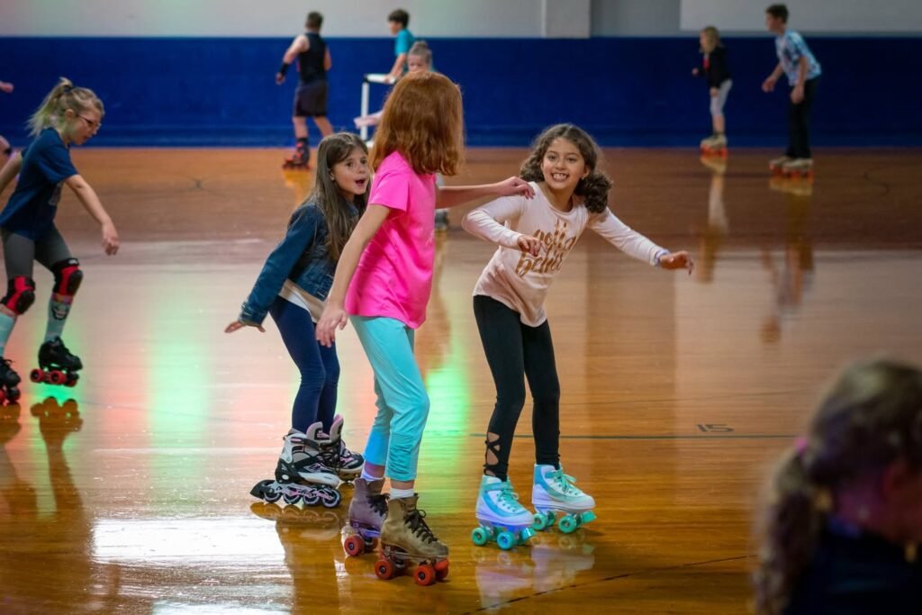 Children practice roller skating in a gymnasium with colorful lights. Close-up view highlights bright quad skates on a polished wooden floor.