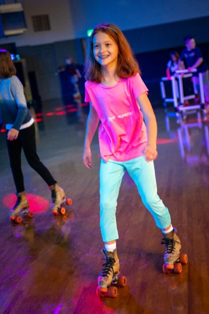 A joyful participant glides across a wooden floor on roller skates in a vibrantly lit rink.