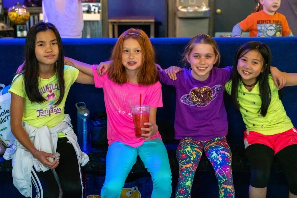 Four young friends sit together in a bowling lounge and share happy smiles.