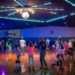 Pusheen’s Birthday People skating on a roller rink with colorful overhead lighting and a classic disco ball. The polished wooden floor reflects the vibrant light patterns.