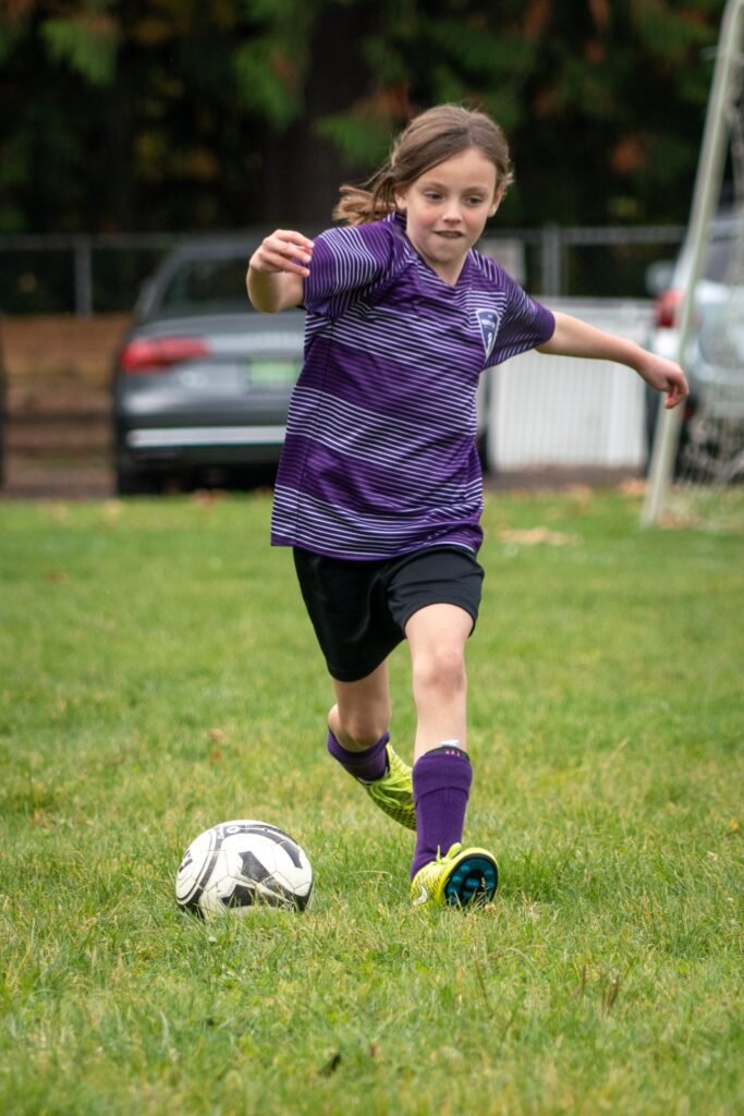 A youth in a purple jersey gets ready to kick a soccer ball on a green field.