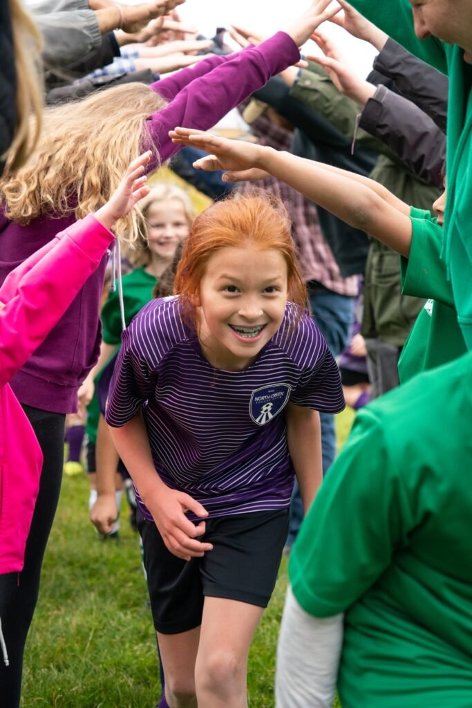 A young soccer player in a purple jersey plays a game of high-five with teammates and coaches on a grassy field.
