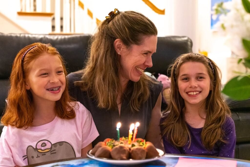 A family enjoys a birthday celebration with a cake and candles in a cozy home setting.