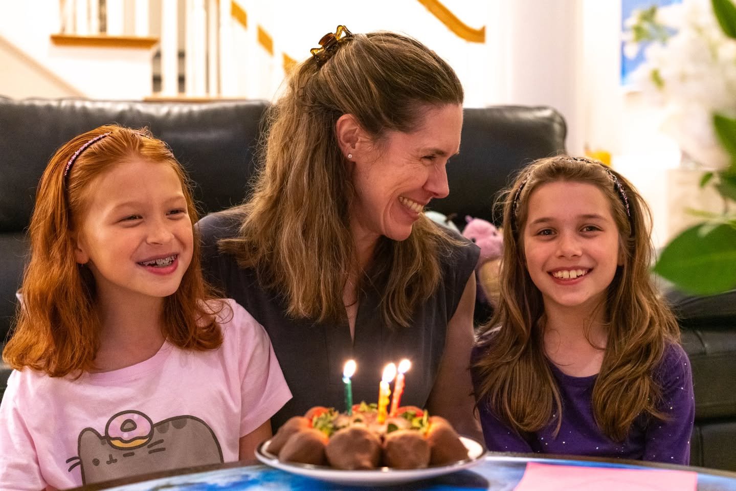 A family enjoys a birthday celebration with a cake and candles in a cozy home setting.