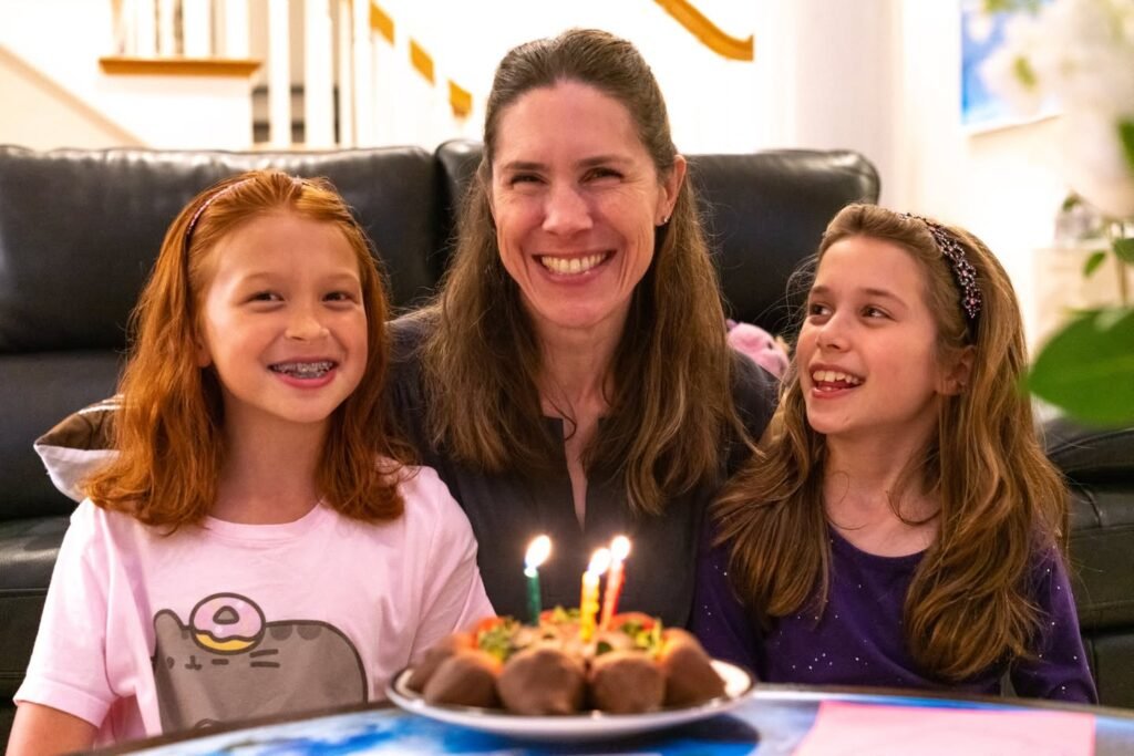 A family gathers around a birthday cake with candles, smiling in a cozy living room.